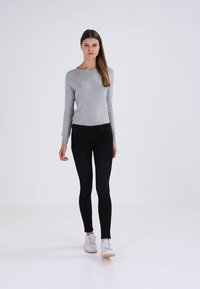 Top gris de manga larga combinado con jeans ajustados negros y zapatillas blancas; textura suave con un diseño ajustado. Fondo liso.