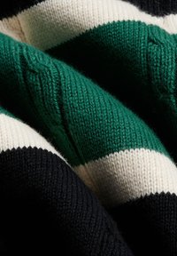 Zbliżenie na złożoną dzianinę z grubymi poziomymi paskami w kolorach czarnym, białym i ciemnozielonym.