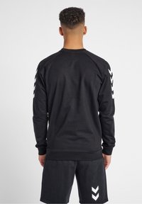 Sudadera negra de manga larga con mangas raglán, con patrones de chevron blancos en los brazos. Tela suave con puños y dobladillo acanalados.