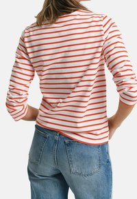 Red and white striped long-sleeve shirt, cotton fabric, relaxed fit, round neckline, paired with blue denim jeans.