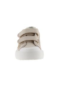 Zapato de lona beige con suela de goma blanca, doble tira de Velcro y un logo verde en la lengüeta. Punta redondeada y parte superior texturizada.