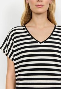 Sort-hvide stribede top med V-udskæring og korte flæseærmer. Stoffet har en ribbet tekstur og har vekslende tykke og tynde striber.