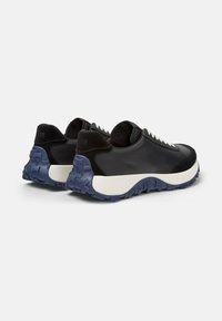 Scarpe da ginnastica nere e blu con suole texturate e lacci bianchi, esposte da dietro per mettere in risalto il design e i materiali.