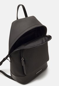 Zaino in pelle nera texturizzata con un ampio interno, tasca anteriore con zip e manico superiore. Branding sottile sul pannello anteriore.