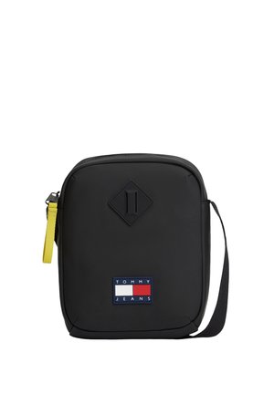 Bolso bandolera negro Tommy Jeans con forma rectangular, parche con logo en la parte frontal, tirador de cremallera amarillo y correa de hombro ajustable.