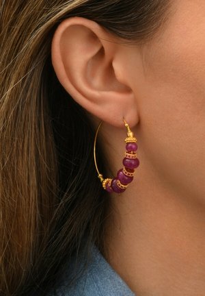 Boucle d'oreille en or avec des perles violettes et des accents décoratifs. La boucle est fixée à un fil d'or fin, amplifiant son design audacieux.