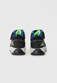 Par de tênis pretos impermeáveis com forro azul e verde neon, vistos de trás sobre um fundo branco.