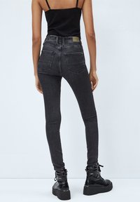 Slim-fit mörkgrå jeans med hög midja och bakfickor, båda med en svart linne och svarta plattform ankle boots.