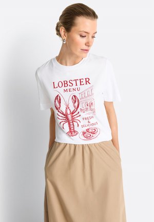 Kontyba fogott hajú nő, fehér pólót visel, melyen piros homár és a „Lobster Menu Fresh & Delicious” felirat található, bézs szoknyával párosítva.