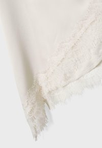 Tissu blanc doux orné d'une délicate bordure en dentelle florale avec de fines franges le long du bord, présenté sur un fond clair uni.