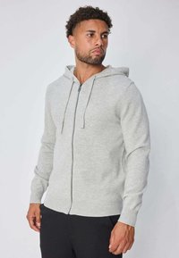 Sweat à capuche gris clair à fermeture éclair, fabriqué en matière douce, avec capuche, manches longues et poignets côtelés. Design simple avec une fermeture éclair à l'avant.