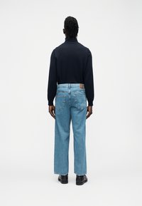 Tumesinine pikkade varrukatega pluus, millele on kombineeritud helesinised laiade jalgadega teksapüksid. Omadusteks on kõrge krae, tagataskud ja pruun vöökohal olev silt.