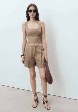Haut en lin brun coupé et short avec un décolleté carré, associé à des sandales brunes à lanières et un sac à main assorti. Lunettes de soleil sombres.