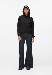 Sweatshirt preto com capuz e laterais ajustadas, combinado com jeans flared azul escuro com aberturas de fenda e botas pretas com atacadores.