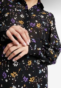 Blusa nera floreale con motivi di fiori viola, gialli e blu; tessuto leggero, polsini con bottoni e design del colletto classico.