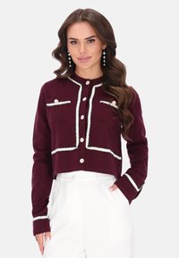 Cárdigan burdeos recortado con ribete blanco, que presenta cierres de botones, dos bolsillos en el pecho y mangas largas. Textura de tela suave.