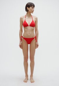 Bikini rosso con top triangolare a sottili spalline e slip a vita bassa con chiusure laterali a nodo. Tessuto dalla texture liscia.
