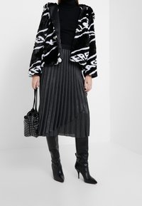 Chaqueta de piel sintética en blanco y negro, suéter de cuello alto negro, falda metálica plisada, botas negras de tacón alto hasta la rodilla y un bolso negro con tachuelas.