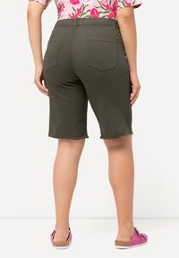Olivově zelené bermudy s roztrhaným lemem, obsahující zadní kapsy a elastický pas. V kombinaci s růžovými nazouvacími botami.
