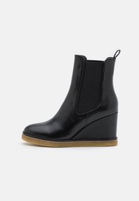 Botte cheville en cuir noir à talon compensé avec des panneaux élastiques sur les côtés et une languette. Bout rond, texture lisse et semelle en caoutchouc beige.