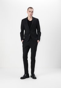 Zwarte op maat gemaakte suit met een slim fit, voorzien van een jasje met één knoop, bijpassende broek en glanzende zwarte dresschoenen. Soepele stoftextuur.