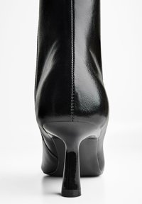 Zwarte enkellaarsjes met hak van glanzend leer, met een slanke vorm, pointed toe en een hoge stilettohak met subtiele stikseldetails.