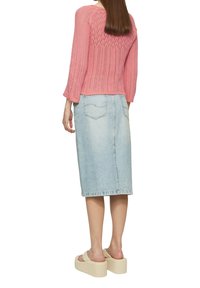 Rosa gestrickter Pullover mit strukturiertem Rücken, kombiniert mit einem hellblauen Jeans-Midirock. Das Model trägt beigefarbene Plateausandalen.