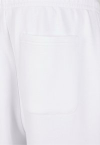Witte sweatpants met een enkele achterzak en stikseldetails. De stof heeft een gladde, zachte textuur. Elastische tailleband zichtbaar aan de bovenkant.