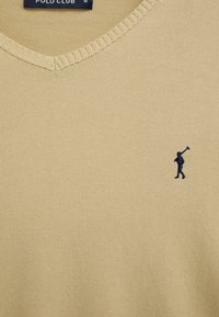 Pull tricoté beige à col en V avec petit logo joueur de polo brodé en bleu foncé sur la poitrine et étiquette "Polo Club" à l'intérieur du col.