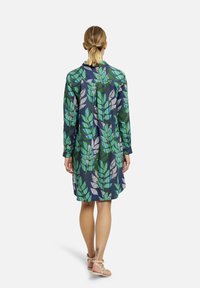 Abito camicia floreale con maniche lunghe, caratterizzato da un motivo di foglie verdi su sfondo blu navy. Realizzato in tessuto leggero, di lunghezza al ginocchio, vestibilità comoda.