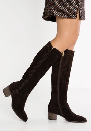 Benen met zwarte suède kniehoge laarzen met blokhakken en ritssluitingen aan de zijkant, gecombineerd met een patroonrok.