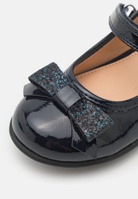 Laková černá bota s kulatou špičkou a lesklým povrchem. Ozdobena černou a modrou třpytivou mašlí.