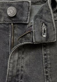 Grå denimtyg med en synlig dragkedja, metalldroppe och sömmar. Har ett slitna område nära knappen och en ficköppning.