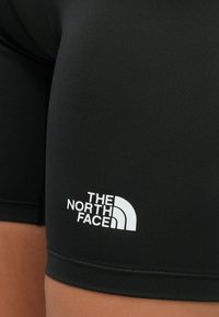 Primo piano di pantaloncini in tessuto nero con il logo bianco The North Face stampato vicino all'orlo sulla coscia di una persona.