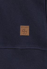 Navyblauw gemêleerd stoffen sweatshirt met ribgebreide accenten en een bruine leren label met "KEY LARGO" en logo erop gestikt.