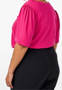 Fuchsia krátký rukáv top s nabíranými rukávy, s kulatým výstřihem, nošený s černými kalhotami na elastický pas. Texturovaná látka s jemnými tečkami.