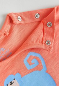 Korallefarbendes Kurzarm-Babyshirt mit silbernen Druckknöpfen, ausgestattet mit einem blauen Affen-Graphic und einem strukturierten Stoff mit einem subtilen Muster.