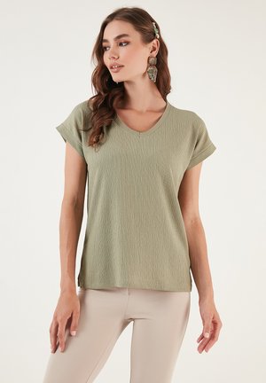 V-neck, short-sleeve top in textured olive green fabric, relaxed fit, paired with light beige leggings. No notable patterns or hardware details.