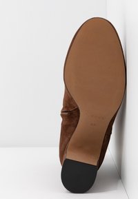 Chaussure en daim marron avec une semelle lisse, un bout arrondi, un léger détail froncé sur la tige, et un accent de talon en caoutchouc noir. Taille 37 imprimée à l'intérieur.
