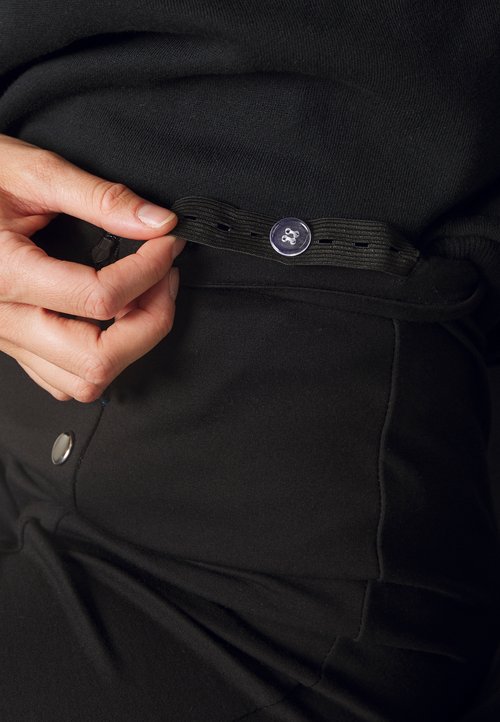 Fekete, rugalmas anyag közeli felvétele, amelyen állítható derékpánt látható gombbal és elasztikus részletekkel; sima, fényes felület.