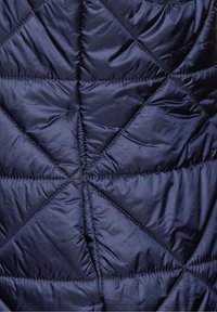 Gestepptes navyblaues Pufferjacken-Material mit diagonalen Nähten, das eine glatte, glänzende Textur und ein geometrisches Muster aufweist.