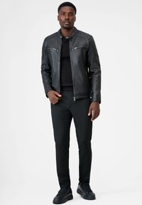 Zwarte leren motorjack met gequilt accenten, ritsborstzakken en een getailleerde snit, gecombineerd met zwarte broek en sneakers.