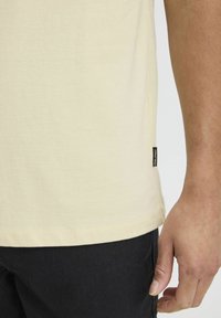 Kortærmet, lysegul T-shirt med en glat tekstur og side-logo, parret med sorte shorts. Ren skæring uden synlige mønstre.