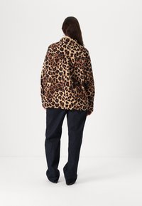 Giacca oversize con stampa leopardata in tessuto morbido, con colletto a scialle, maniche lunghe e vestibilità rilassata, abbinata a pantaloni in denim scuro.