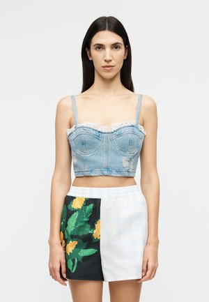 Νεαρή γυναίκα με ίσια σκούρα μαλλιά που φοράει crop top από φθαρμένο τζιν και σορτς με ψηλή μέση, με μαύρα, λευκά και φλοράλ πάνελ.