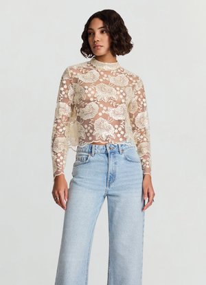 Top in pizzo a maniche lunghe color avorio con motivi floreali, collo alto e orlo smerlato, abbinato a jeans a gamba larga color azzurro chiaro.