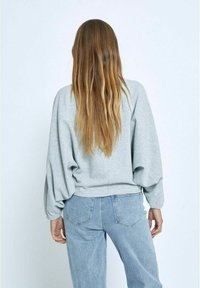 Grauer, übergroßer Pullover mit geripptem Textur, Ballonärmel und einem leicht verkürzten Saum, kombiniert mit hellblauen Jeans.