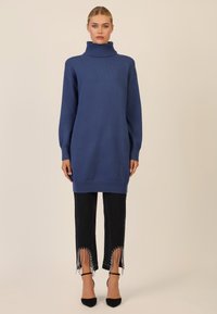 Niebieski sweter z golfem, w oversize'owym fasonie, z długimi rękawami. Zestawiony z czarnymi dżinsami z frędzlami i zdobieniami u dołu.