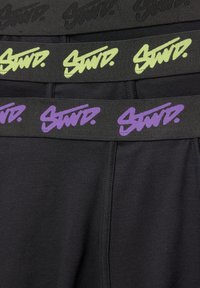Leggings negre cu trei curele ajustabile în negru, verde și mov, fiecare având textul "STWD" într-un font îndrăzneț și stilizat.