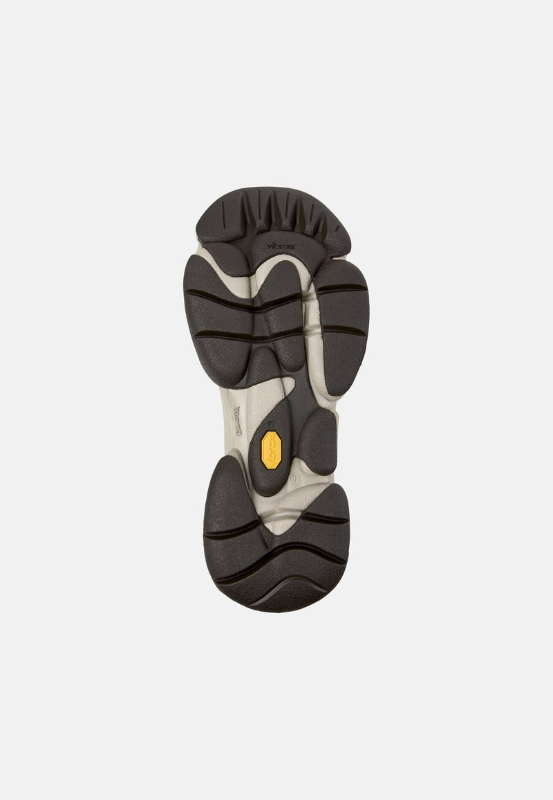 Semelle extérieure Vibram avec un profil en caoutchouc noir multdirectionnel, accents blancs, forme contournée et rainures prononcées pour une meilleure adhérence.